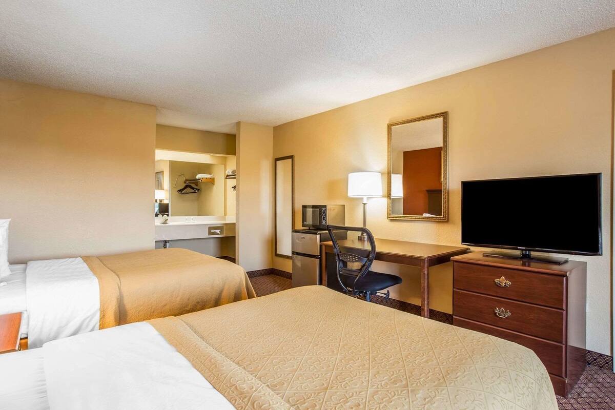 A hotel room with two beds, a desk, a television, and a mirror.