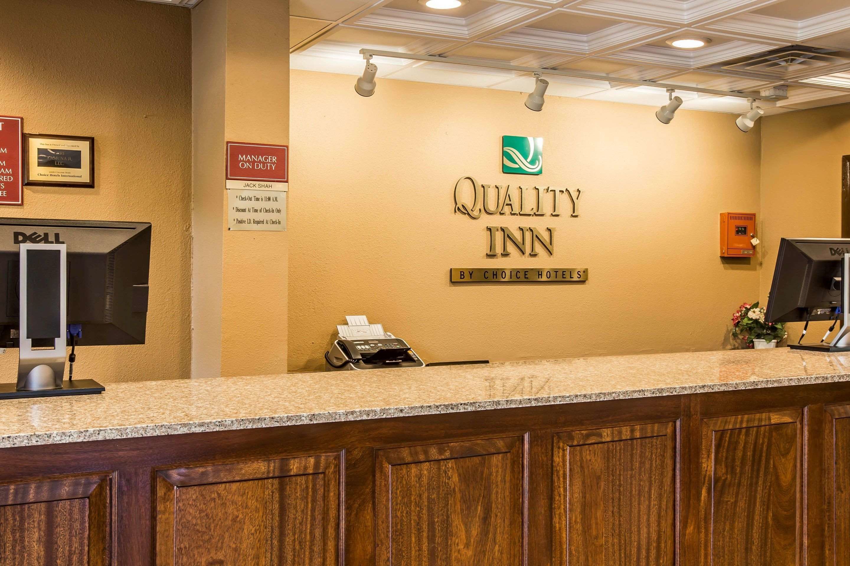 Mostrador de recepción en Quality Inn con una computadora Dell, un teléfono y un letrero que dice 'Gerente de Guardia'.