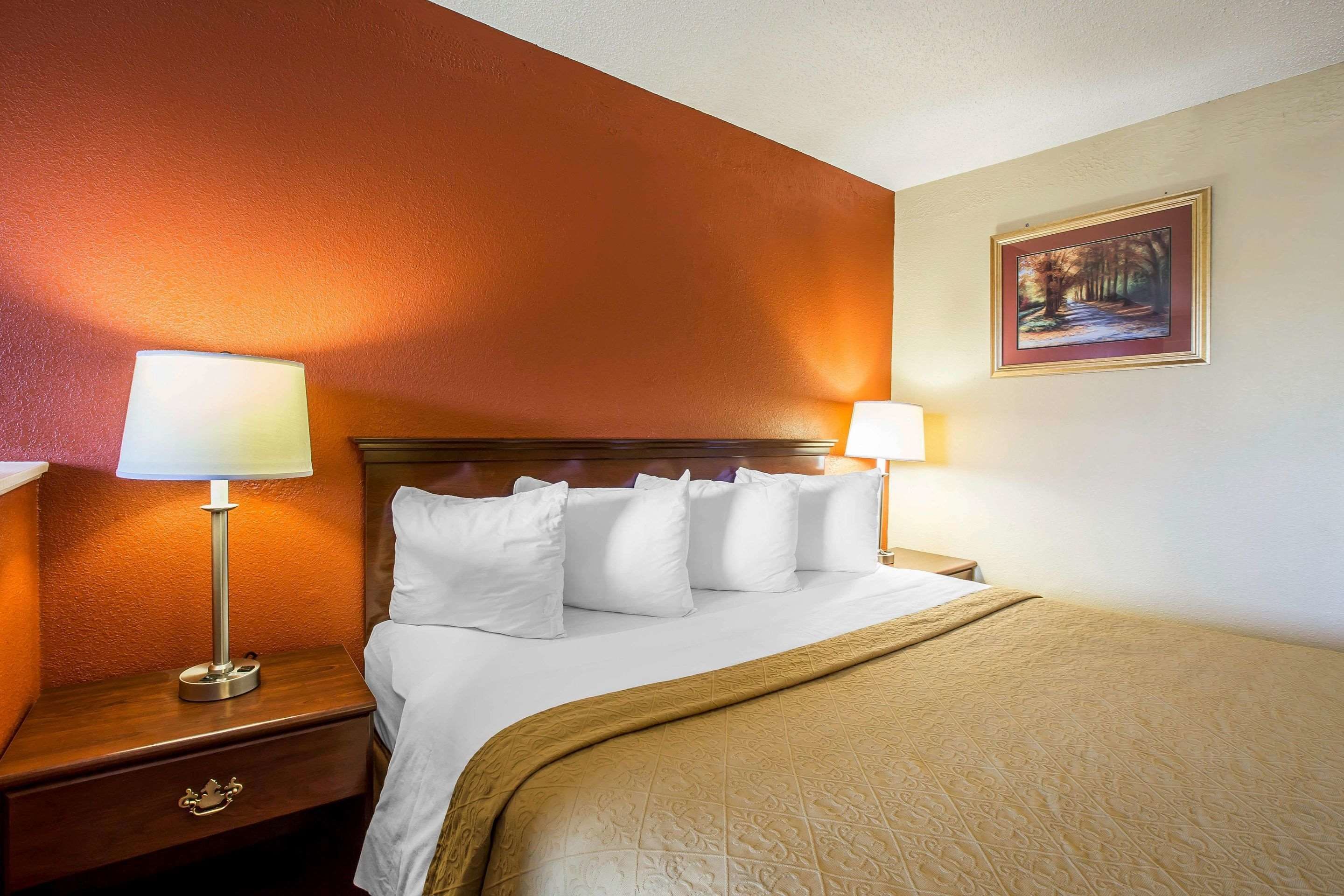 A hotel room with a bed, two bedside tables with lamps, a nightstand with a drawer, and a framed picture on the wall.