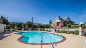 A swimming pool with a brick border and a metal ladder, surrounded by a fence and a house in the background. - Quality Inn Gaffney I-85 (Gaffney)