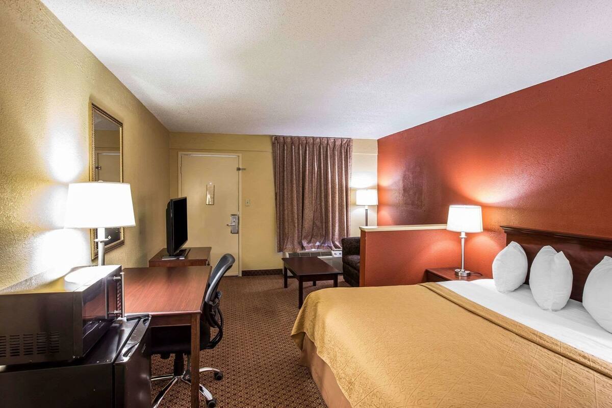 A hotel room with a bed, desk, chair, television, and two lamps.