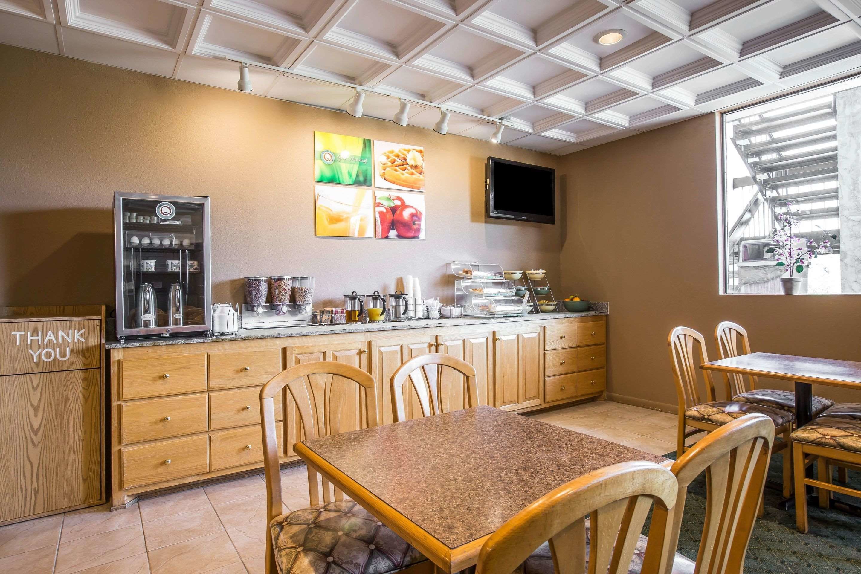Una cocina con armarios de madera, encimera de granito, cafetera y televisor montado en la pared.