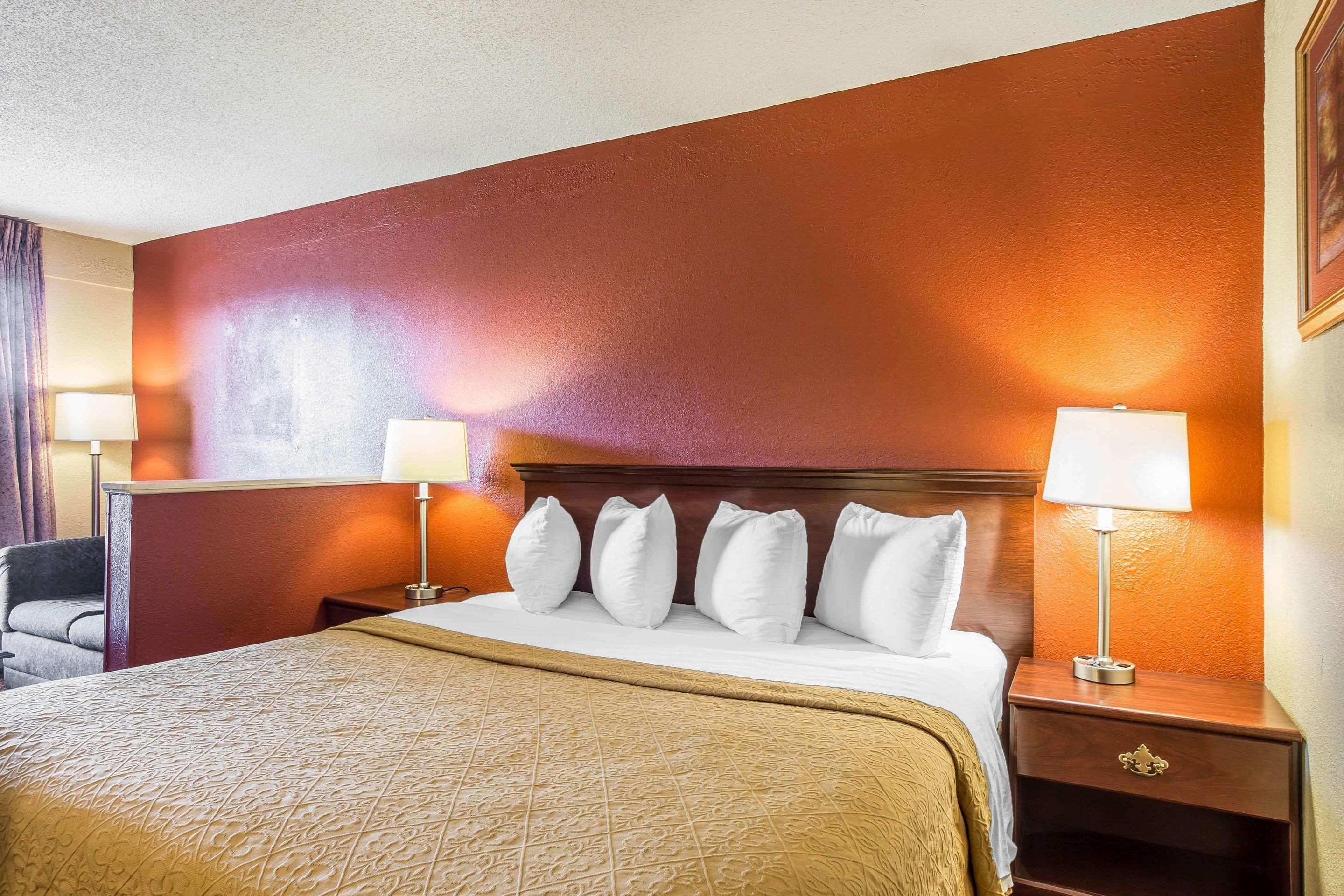 Una habitación de hotel con una cama grande, un cabecero de madera y dos mesitas de noche con lámparas.