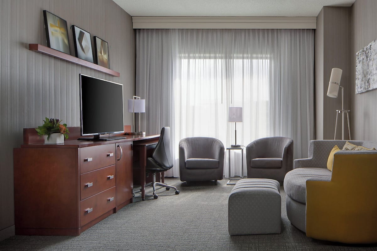 A hotel room with a flat-screen TV, a desk, two armchairs, a sofa, and a small side table.