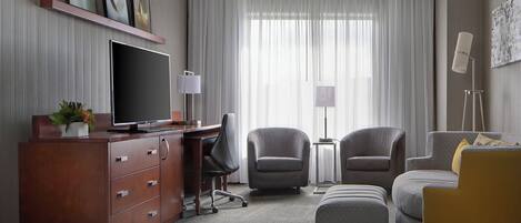 Habitación de hotel con televisión de pantalla plana, escritorio, dos sillones, un sofá y una mesita auxiliar.