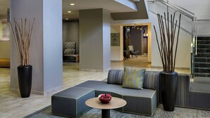 Un moderno vestíbulo de hotel con una escalera curva, zonas de estar y un gran jarrón con ramas.