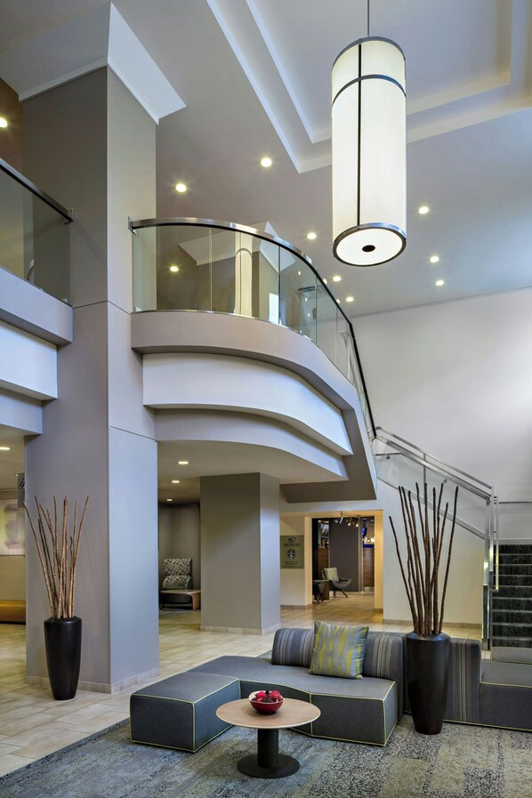 A modern hotel lobby with a curved staircase, seating areas, and a large vase with branches. - Courtyard by Marriott Downtown Grand Rapids (Grand Rapids)