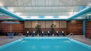 Una piscina interior con techo de tragaluces, paneles de madera y varias sillas de descanso.
