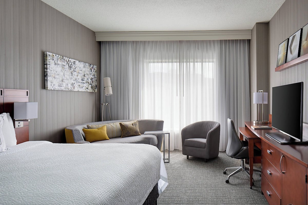 A hotel room with a large bed, a desk with a TV, a chair, and a painting on the wall.