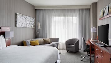 Quarto de hotel com uma cama grande, uma escrivaninha com televisão, uma cadeira e um quadro na parede.