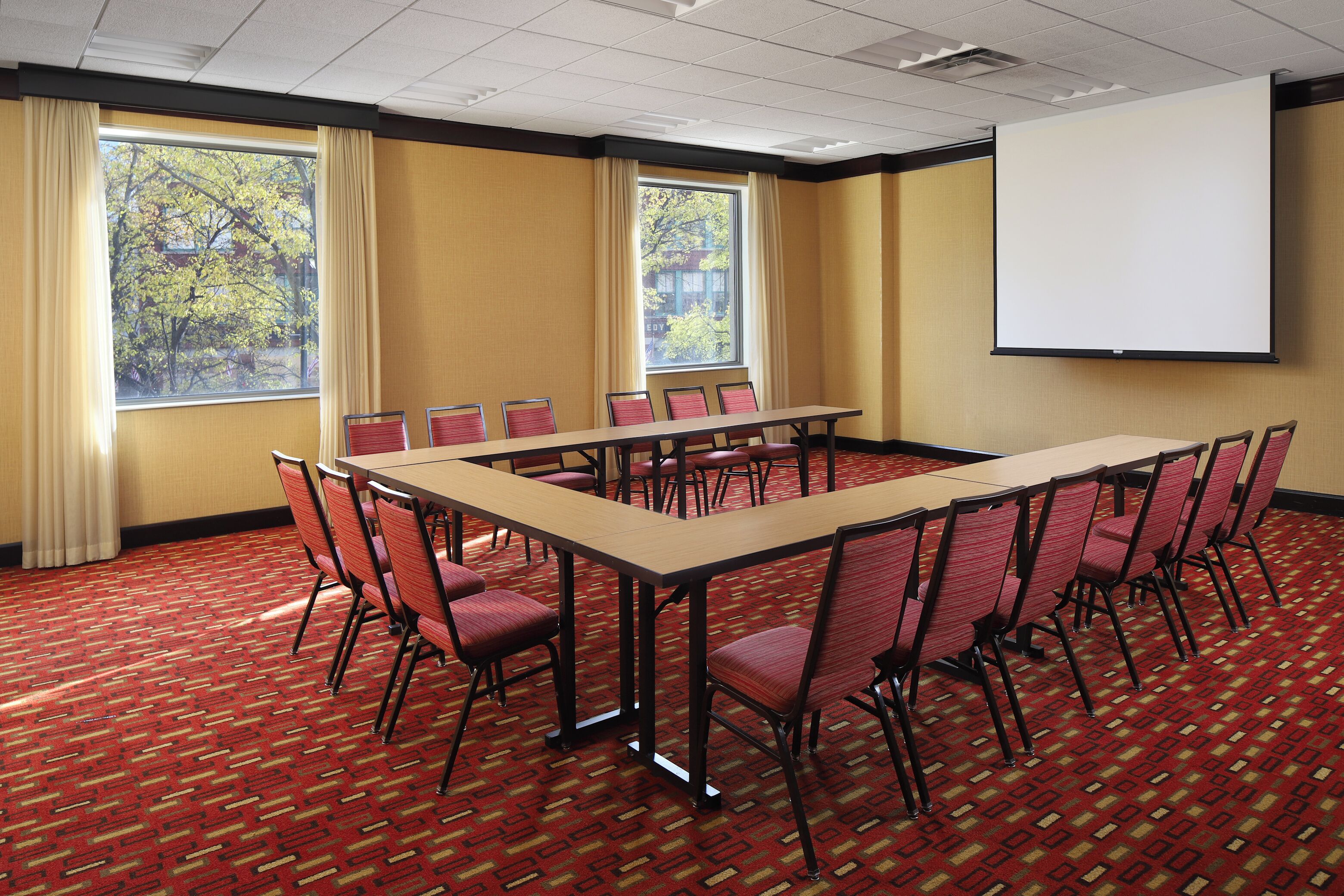 A conference room with a long table, red chairs, and a projector screen.