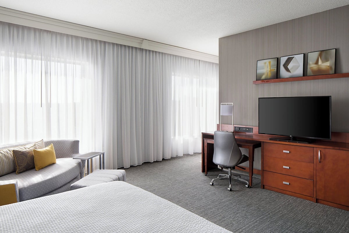 A hotel room with a bed, a desk, a television, and a sofa.