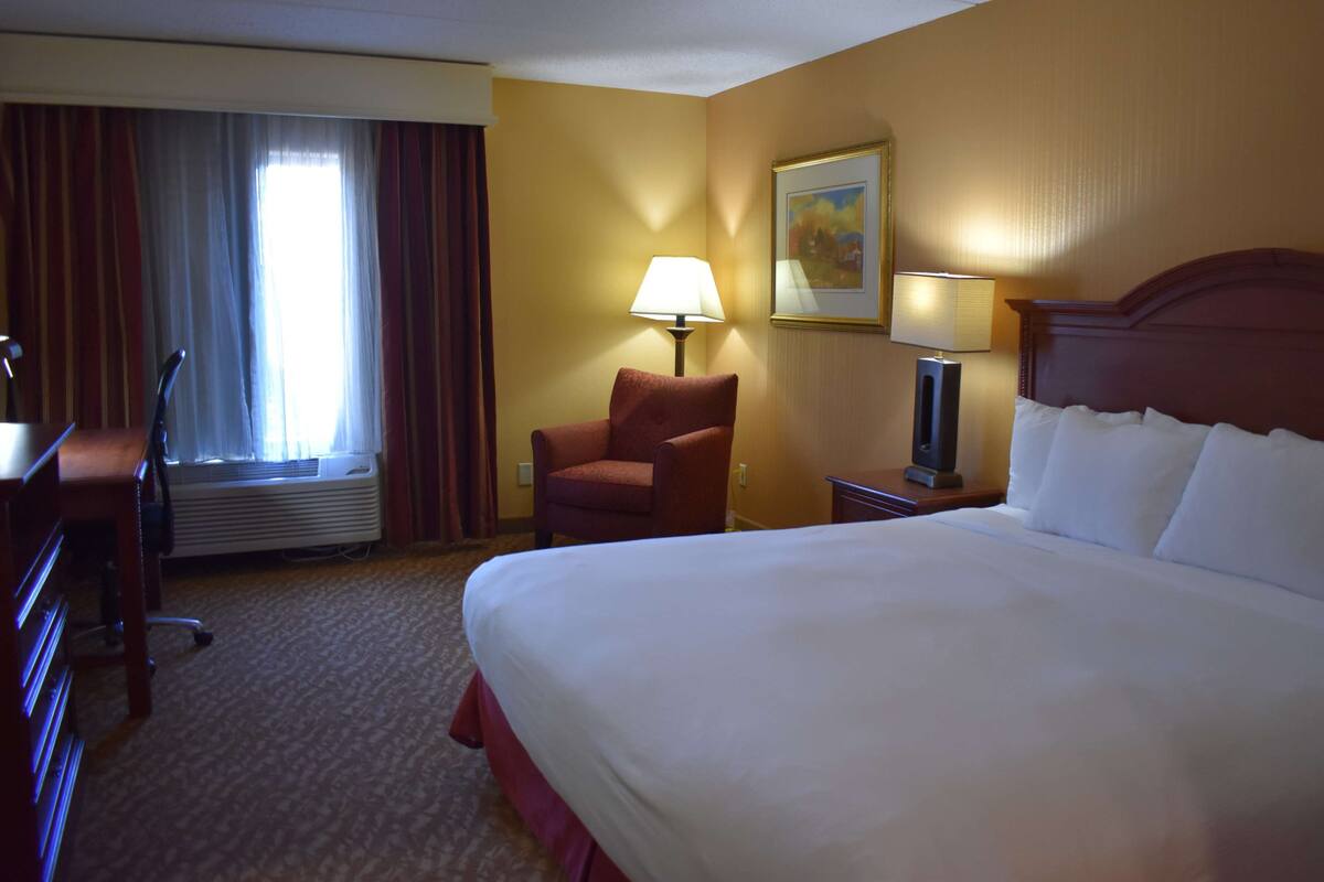 Quarto de hotel com uma cama grande, uma escrivaninha, uma cadeira, um abajur e um quadro na parede.