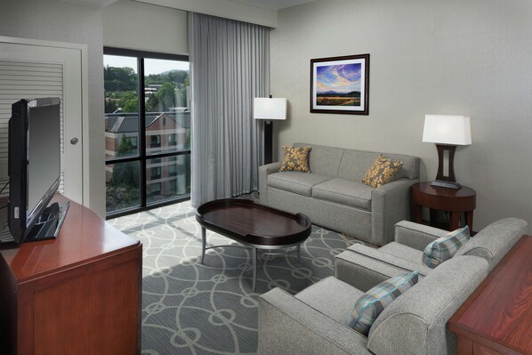 A hotel room with a sofa, a small table, a TV, and a window with curtains.