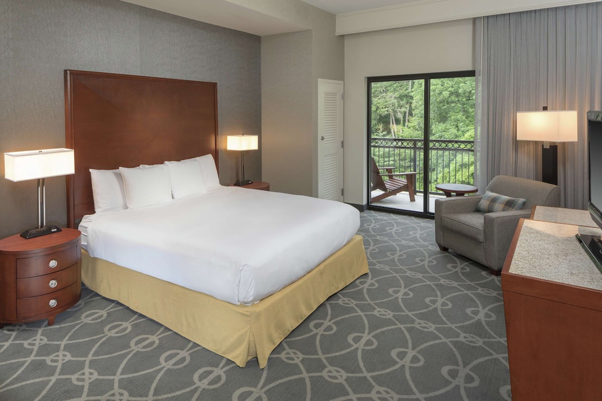 Quarto de hotel com cama grande, escrivaninha, cadeira e varanda com vista para árvores.