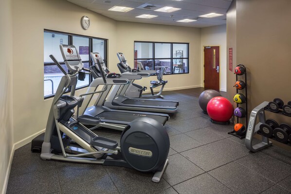 A gym with treadmills, elliptical machines, a large red exercise ball, and a rack of dumbbells.