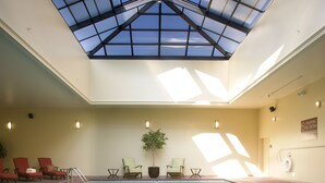 Ein Hallenbad mit Dachfenster, roten Liegestühlen und einer Zimmerpflanze.