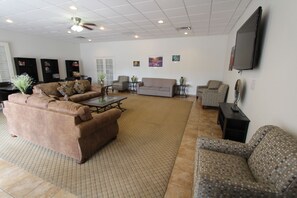 A spacious living room with a brown sofa, patterned armchairs, a coffee table, and a flat-screen TV mounted on the wall. - Desert Breezes Resort (Palm Desert)