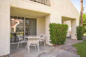 A patio with a table and chairs, a glass door, and a hedge. - Desert Breezes Resort (Palm Desert)
