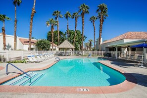 A swimming pool with lounge chairs, palm trees, and a fenced area. - Desert Breezes Resort (Palm Desert)