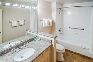 A bathroom with a granite countertop sink, a mirror, and a shower with a grab bar. - Desert Breezes Resort (Palm Desert)
