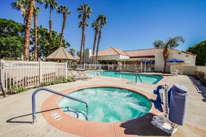 A pool area with a hot tub, lounge chairs, and palm trees.
