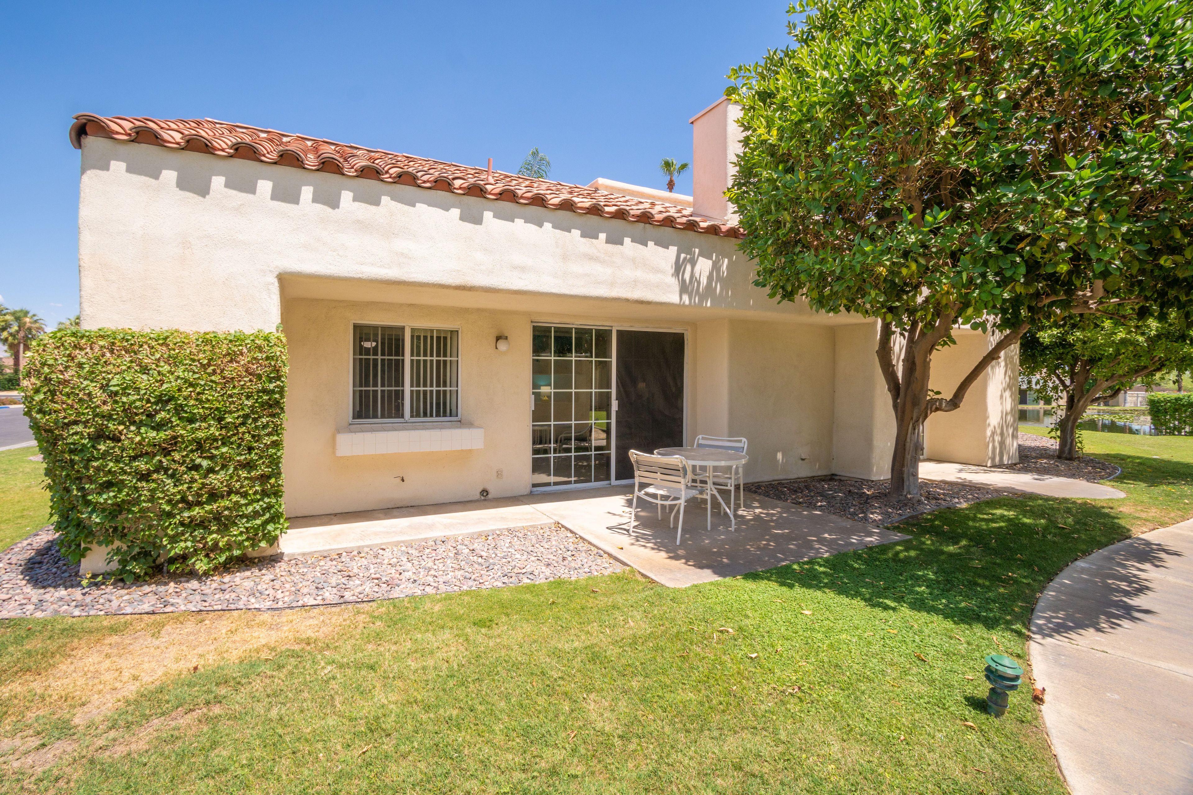 A single-story house with a tiled roof, a covered patio with a table and chairs, and a well-maintained lawn.