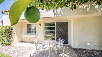 A patio with a table and chairs, a sliding glass door, and a view of a garden.