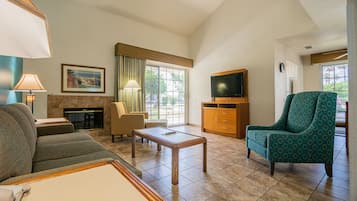 Un salon d’hôtel comprenant un canapé, un fauteuil, une table basse, une cheminée, un téléviseur et une grande fenêtre donnant sur l’extérieur.