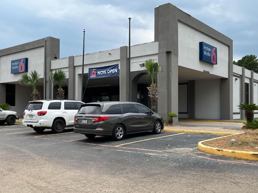 A motel with a 'NOW OPEN' sign, two parked cars, and a parking lot.