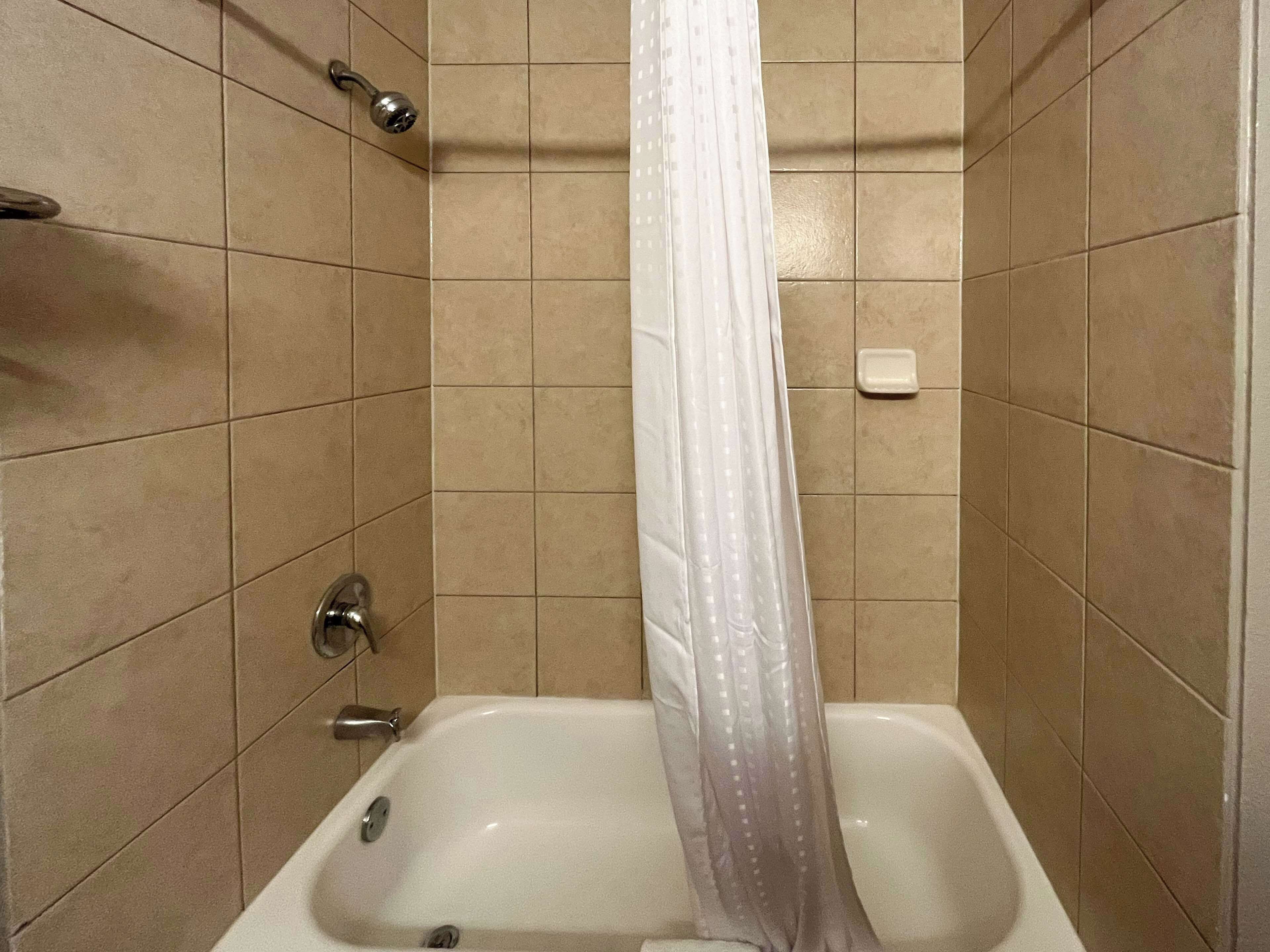 A bathroom with a bathtub, a shower curtain, and a soap dish.
