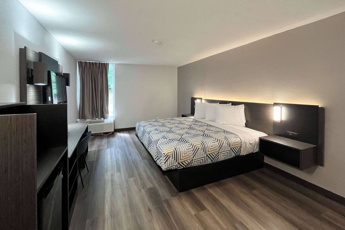 A modern hotel room with a large bed, a desk, and a TV.