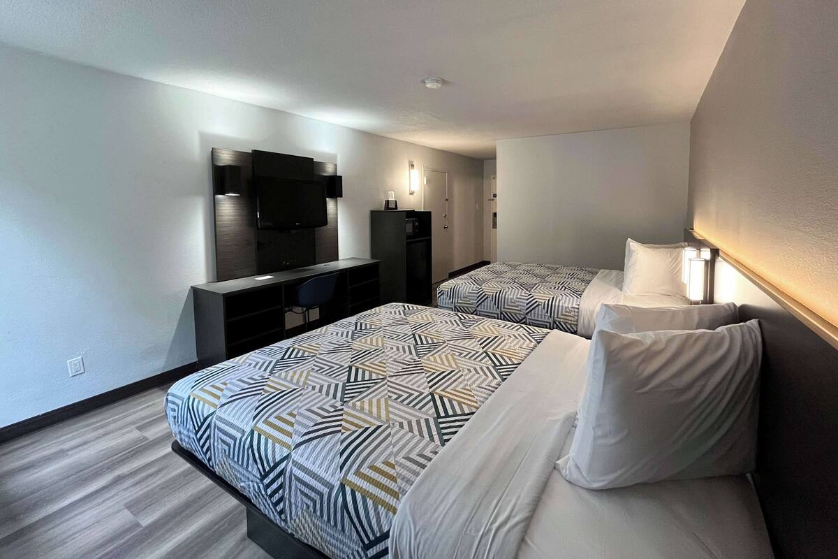 A modern hotel room with two beds, a desk, a TV, and a wardrobe.