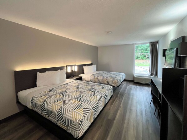 A hotel room with two beds, a desk, and a TV.