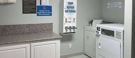 A laundry room with a sink, a soap dispenser, and a warning sign about unattended items.
