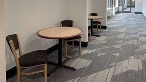 A corridor with carpeted flooring and a series of round tables and chairs. - Motel 6 Nacogdoches, TX-SFA University (Nacogdoches)