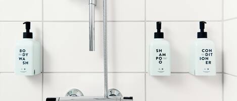 A modern bathroom with a chrome shower, a handheld showerhead, and three bottles of body wash, shampoo, and conditioner.