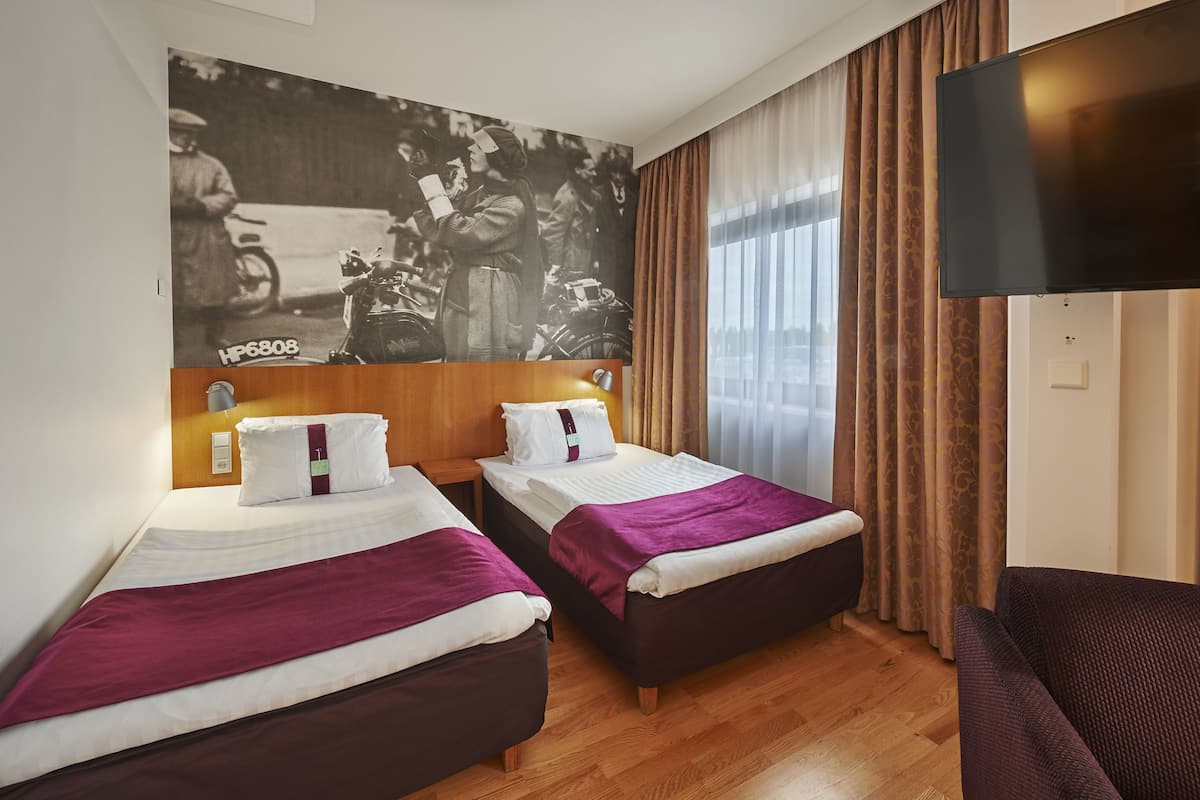 A hotel room with two beds, a large poster on the wall, a TV, and a window with curtains.