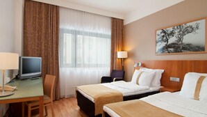 A hotel room with two beds, a desk with a television, a chair, a lamp, and a painting on the wall. - Scandic Veromies (Vantaa)