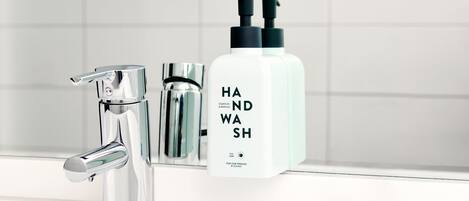 Un baño moderno con un grifo cromado, una botella blanca etiquetada 'HAND WASH' y un dispensador de jabón.
