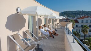A rooftop terrace with sun loungers and umbrellas, overlooking a cityscape. - CRISTAL HOTEL & SPA (Cannes)