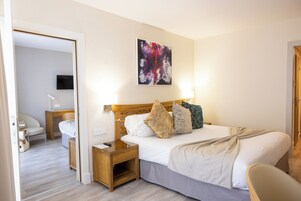 Een hotelkamer met een bed, nachtkastjes, een stoel en een schilderij aan de muur.