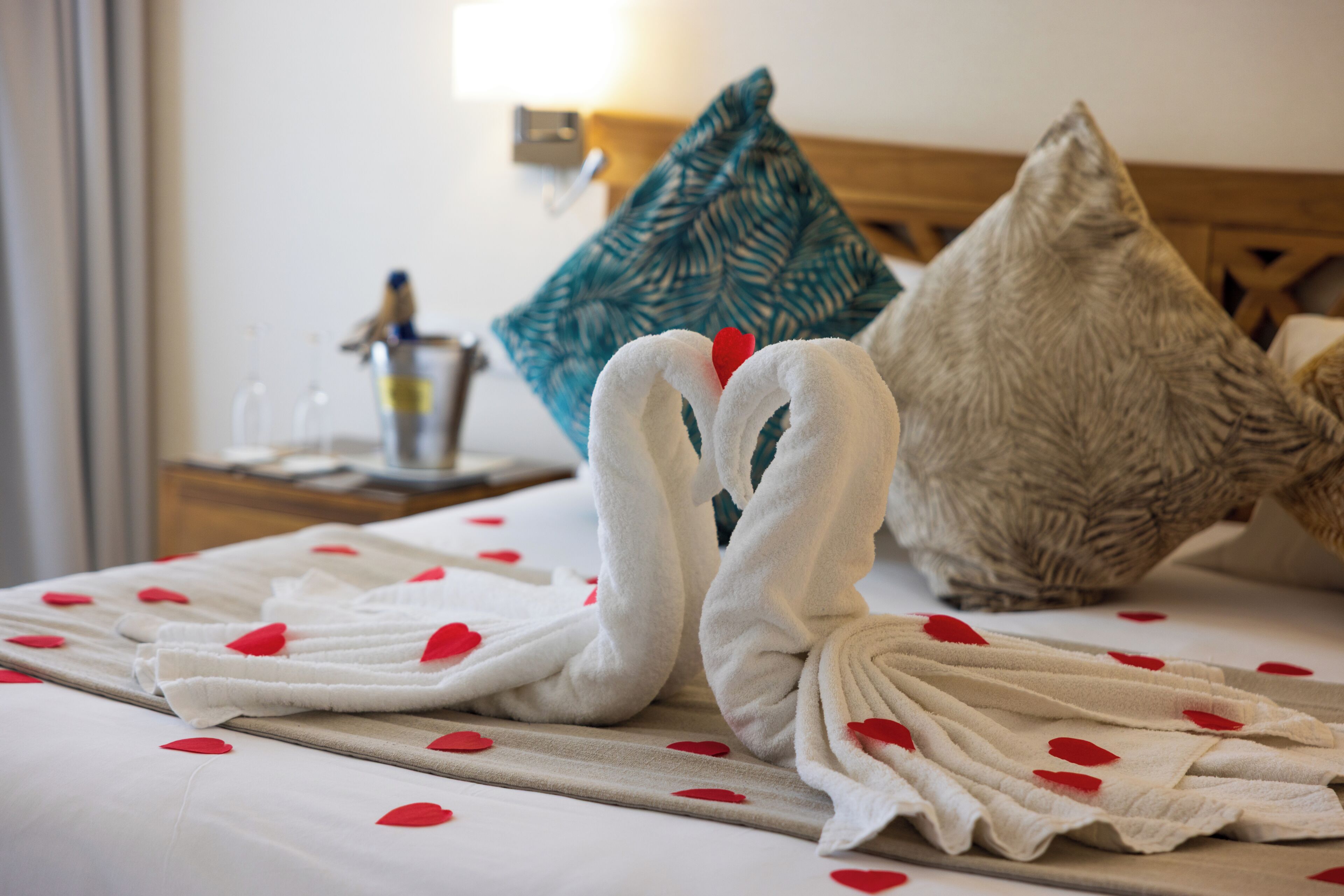 A bed with two white towels arranged in a swan shape, a teal pillow, and a wooden headboard.