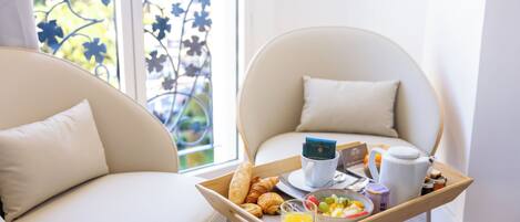 A breakfast tray with croissants, orange juice, and a bowl of fruit on a wooden table between two white chairs with cushions.