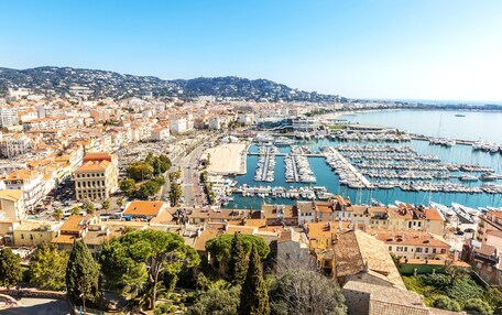 A coastal cityscape with a marina filled with boats, historic buildings, and a hilly backdrop.