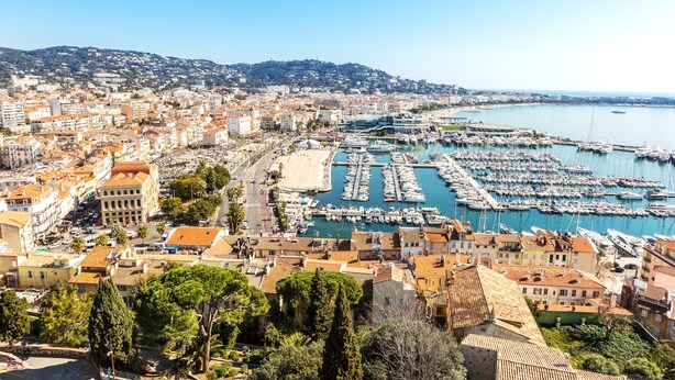 A coastal cityscape with a marina filled with boats, historic buildings, and a hilly backdrop. - CRISTAL HOTEL & SPA (Cannes)