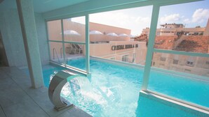 An indoor swimming pool with clear blue water, a diving board, and a view of the surrounding buildings. - CRISTAL HOTEL & SPA (Cannes)