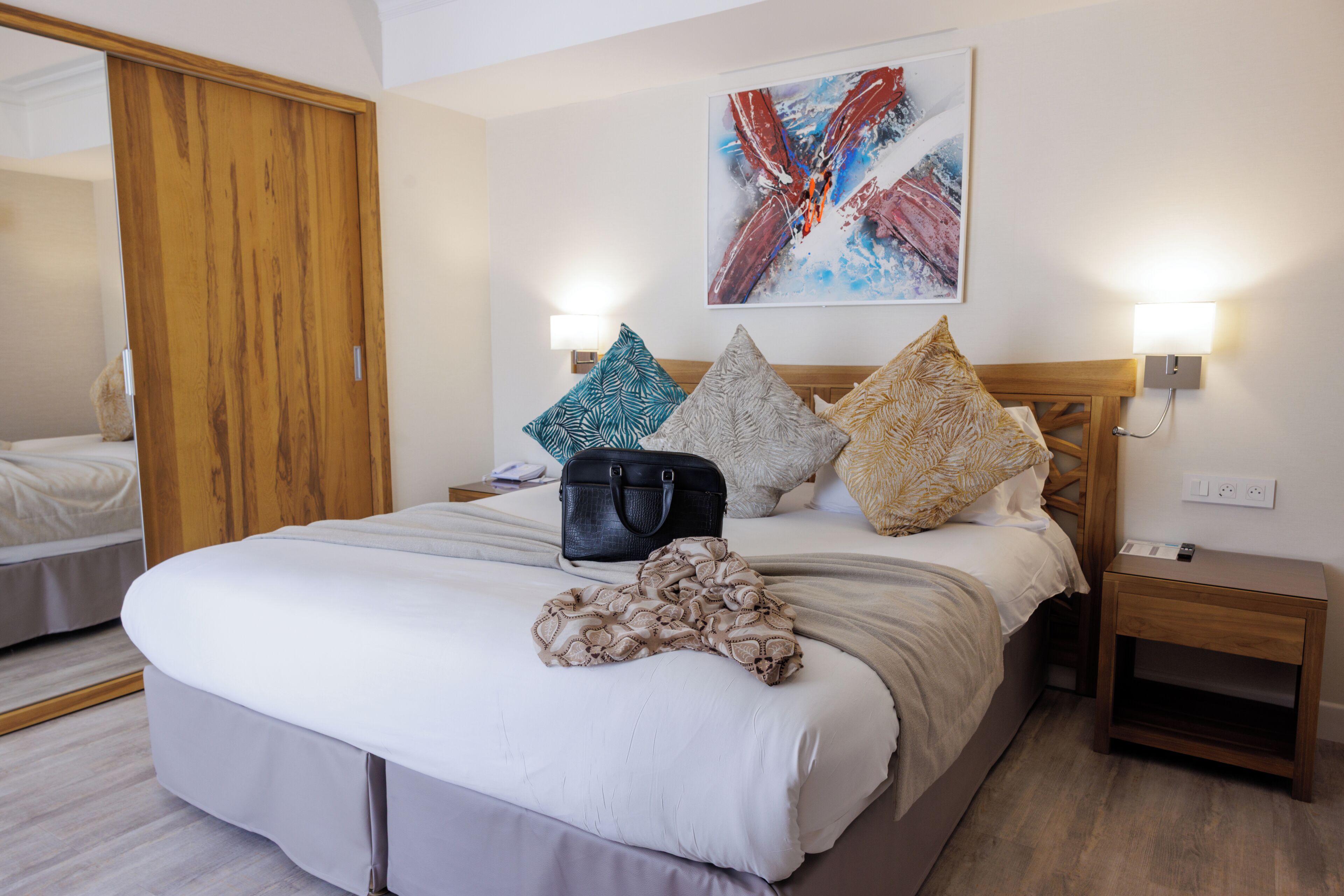 Habitación de hotel con una cama grande, un armario de madera, una mesita de noche con lámpara y un cuadro en la pared.