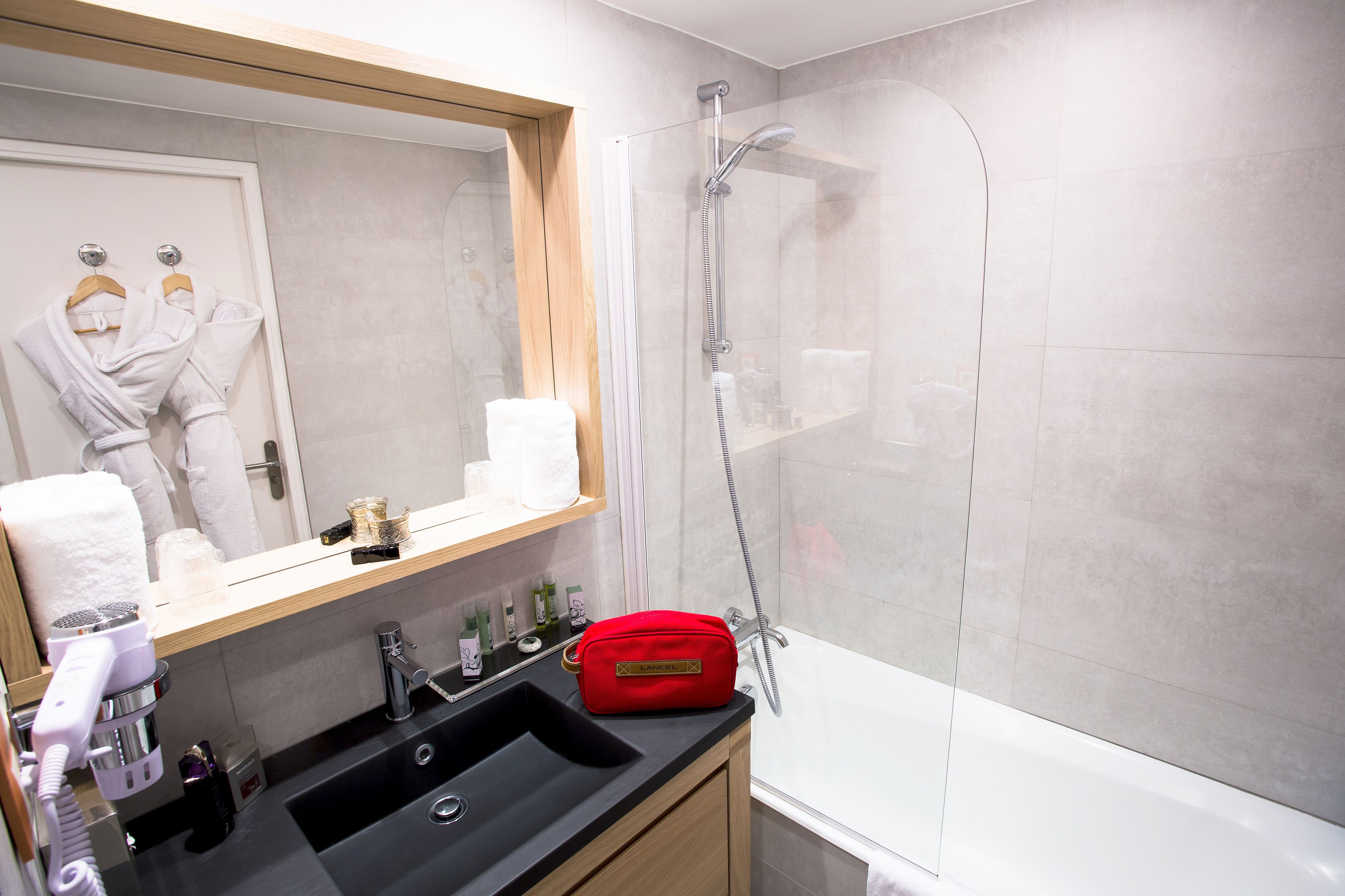 A modern bathroom with a glass-enclosed shower, a sink with toiletries, and a mirror with a robe hanging.