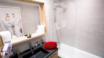 A modern bathroom with a glass-enclosed shower, a sink with toiletries, and a mirror with a robe hanging.